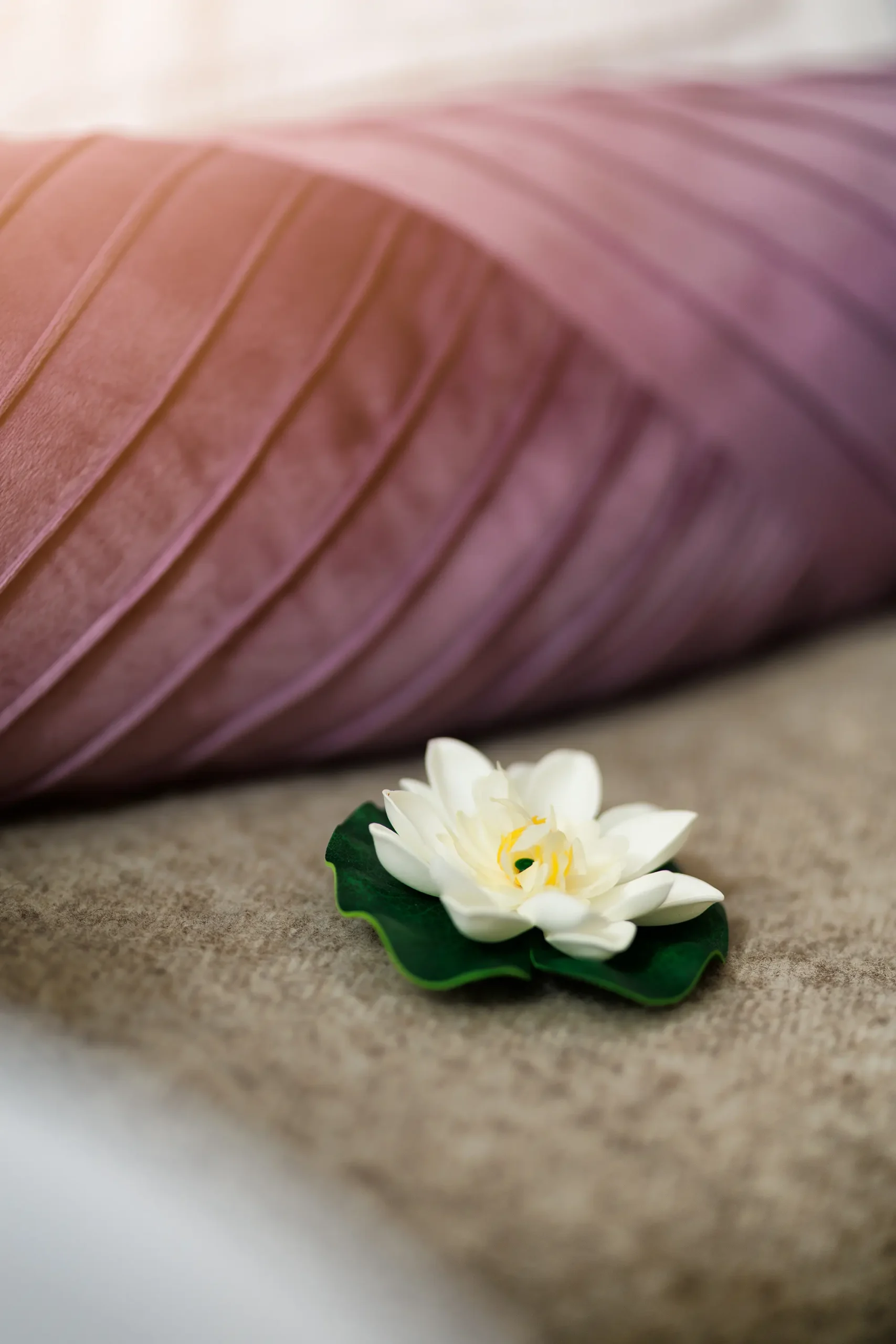 Lila farbenes Kissen und braune Decke, auf der eine weiße Lotusblüte als Dekoration platziert ist